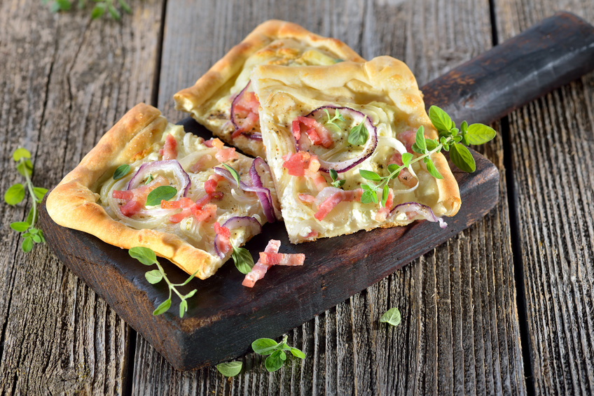 Klassische Elssser Flammkuchen-Schnitten mit Zwiebeln und Speck rustikal auf Holzbrett serviert - Traditional Tarte Flambe from Alsace with onions, bacon and sour cream